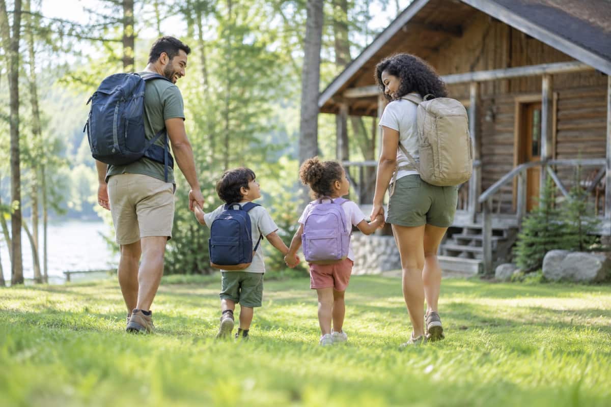 Parents and two small children walking hand in hand toward a camp cabin